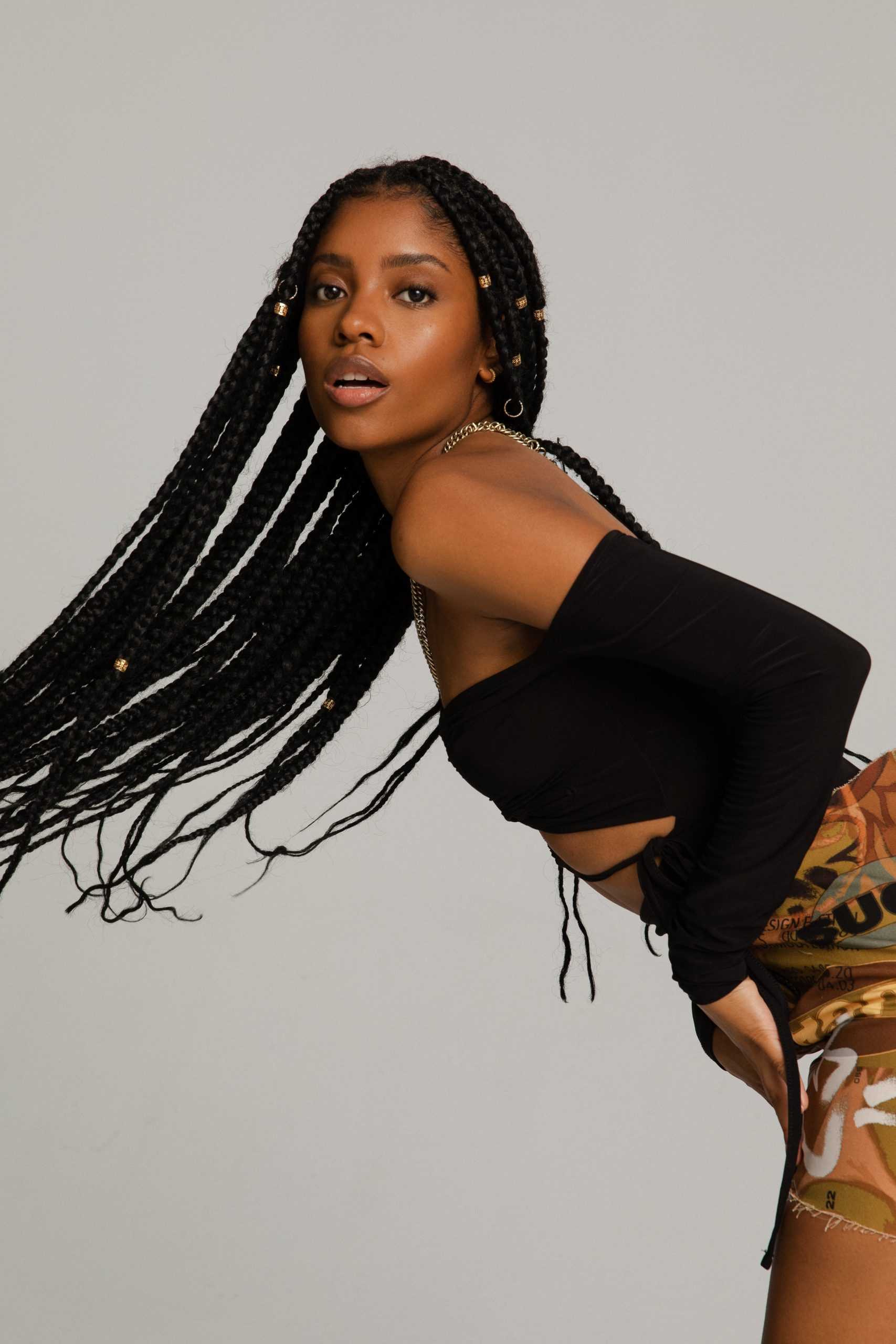 Mann mit weißem Unterhemd, offenen Hemd und braunem Blazer zu beiger Chino posiert.